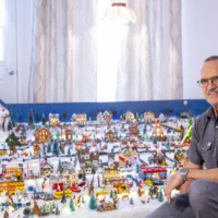 Monsieur Roger Couture assis près de son village miniature de Noël