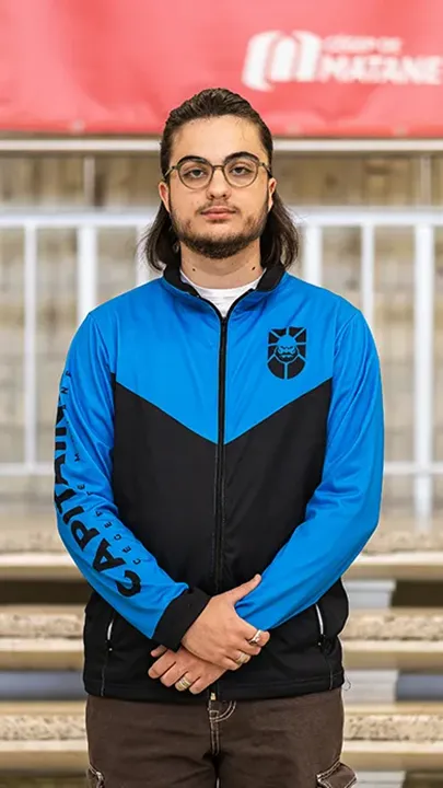 Un athlète de l'équipe de sport électronique pose sur les marches de l'escalier du hall d'entrée du Cégep de Matane pour sa photo d'équipe, vêtu de la veste bleue et noire des Capitaines.