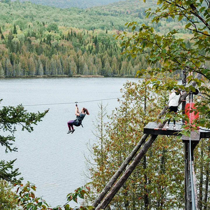 Une étudiante effectue une descente de tyrolienne au-dessus d'un lac et dans un paysage de forêts lors d'un parcours d'hébertisme.