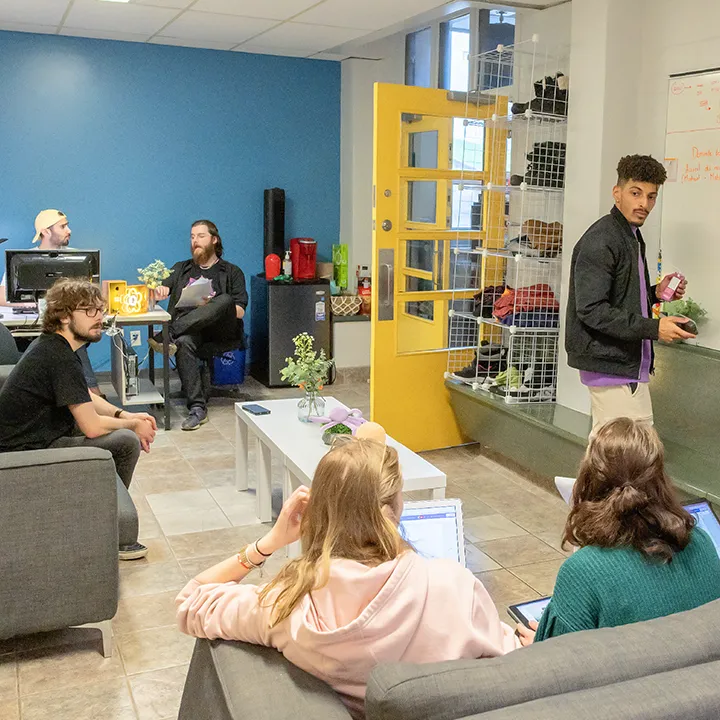 Dans le local de l'association étudiante du cégep, des étudiantes et étudiants discutent, assis sur des canapés ou sur des chaises de bureau. Le groupe semble préparer une activité, en délégant l'un d'entre eux pour prendre des notes sur un grand tableau blanc, comme lors d'une séance de brainstorming.