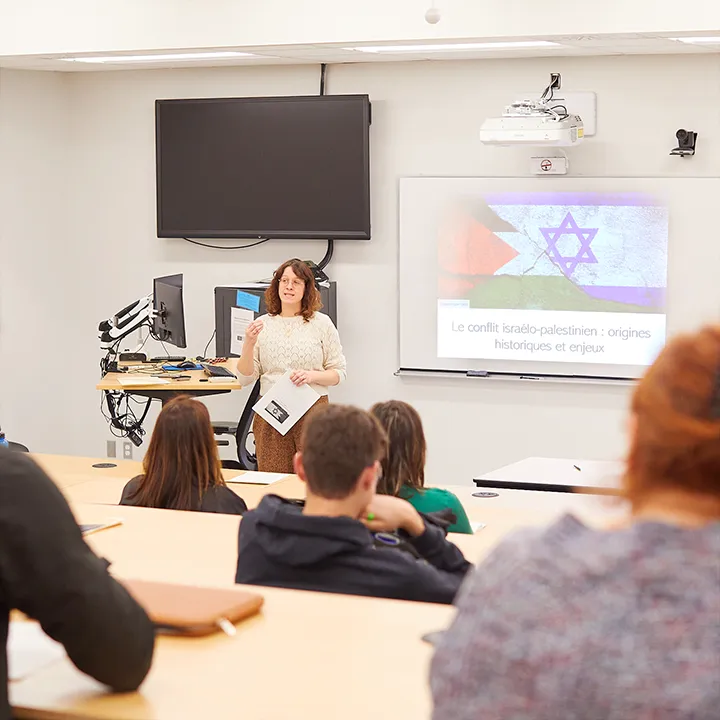 Une enseignante au pied d'un amphithéâtre est en train d'animer devant des étudiantes et étudiants une conférence sur les origines du conflit israélo-palestinien.