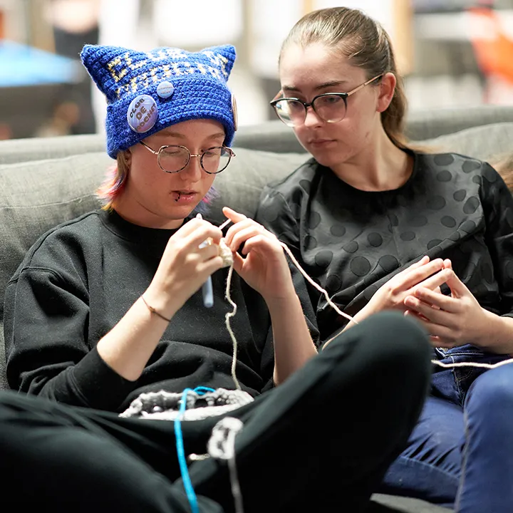 Deux étudiantes assises sur un canapé sont en train de pratiquer une activité de tricot au crochet.