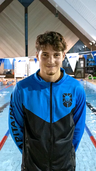 Un athlète des Capitaines, dans une piscine, sur le bord d'un bassin de natation, pose avec la tenue bleue et noire des Capitaines dans le cadre de la photo officielle de l'équipe collégiale de natation.