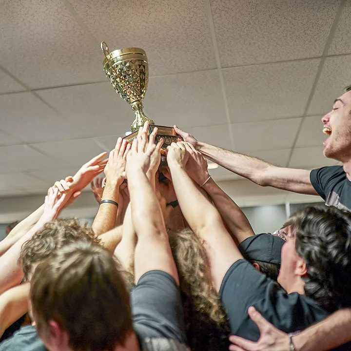 Un groupe d'étudiantes et d'étudiants brandissent dans les airs avec fierté une coupe remportée lors des Olympiades de la vie active.