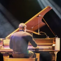 Un étudiant joue du piano sur la scène de la salle Lucien-Bellemare, éclairé par des projecteurs de lumière, assis devant un piano à queue.