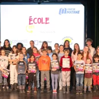 Des élèves du primaire, en compagnie de leurs mentors du cégep, prennent la pose dans le cadre de la remise de leur diplôme de l'École des Grands, sur la scène de l'auditorium du cégep.