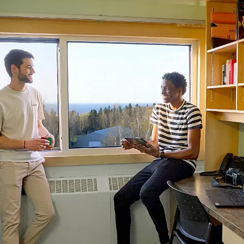 Deux étudiants souriants devant la fenêtre d'une chambre de la résidence étudiante du cégep.